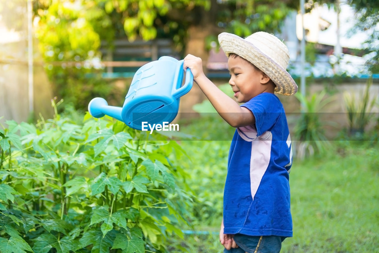Side view of boy watering plants while standing on land
