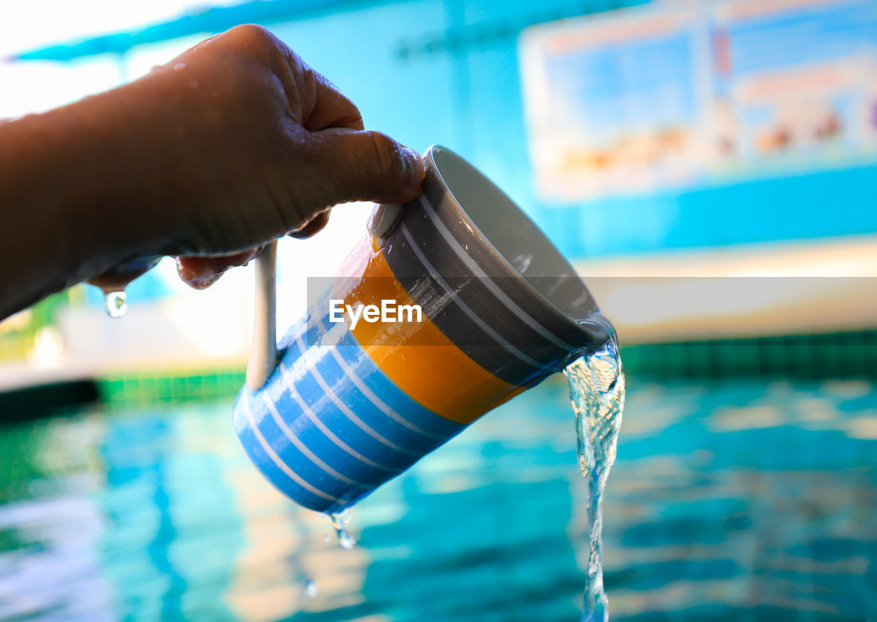 Close-up of hand holding coffee cup by swimming pool