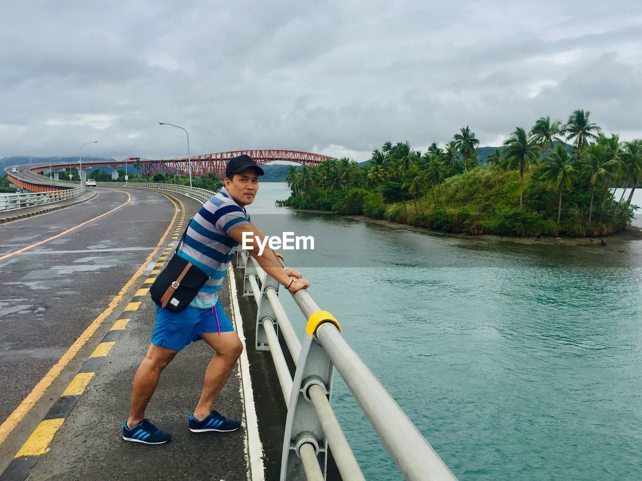 Full length side view of young man standing on bridge over river against sky