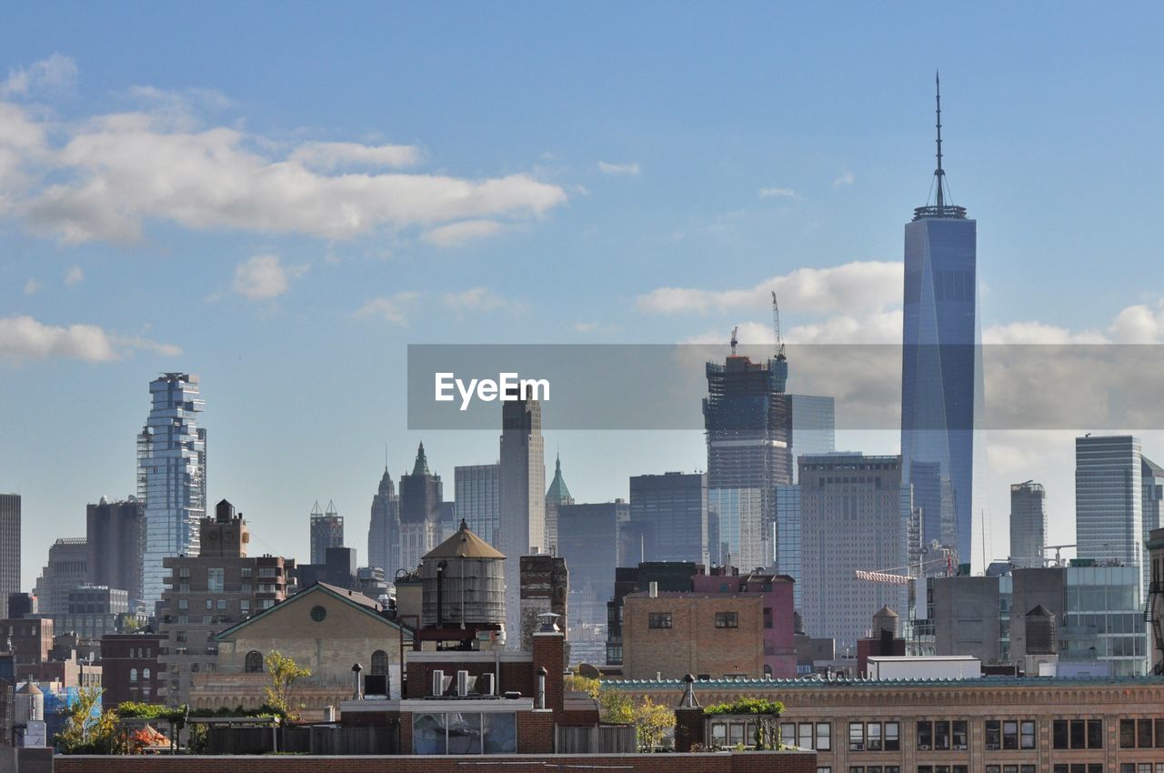 One world trade center by modern buildings against cloudy sky