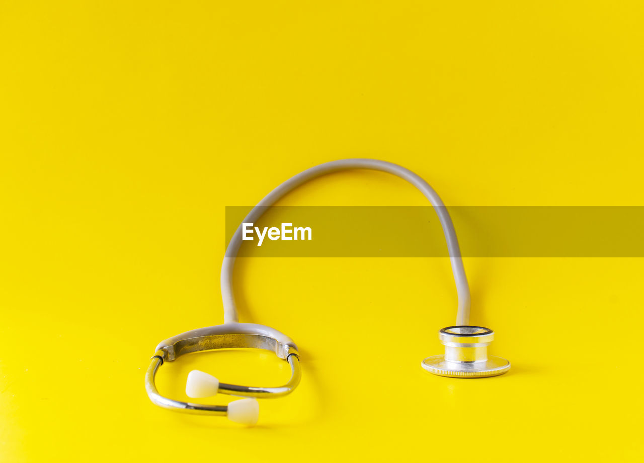 yellow, colored background, studio shot, yellow background, copy space, indoors, metal, no people, cut out, fashion accessory, stethoscope, single object, close-up, medical instrument