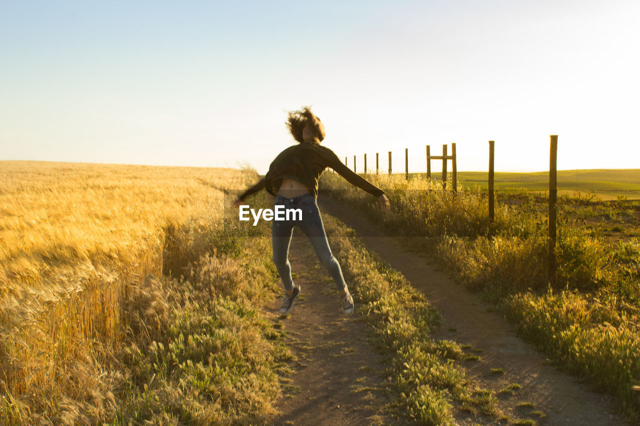 Full length of woman jumping on field against sky during sunset