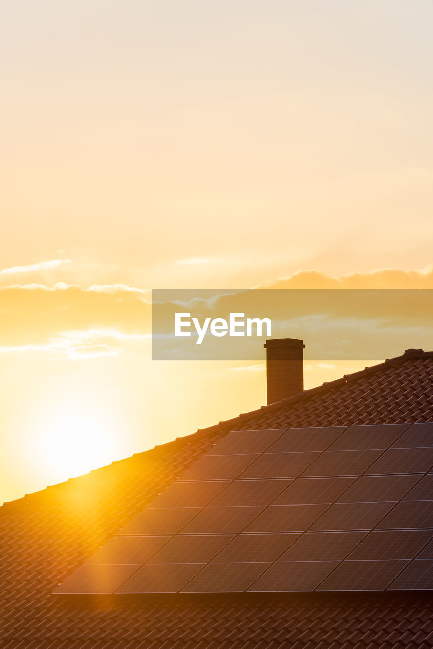 Real photo of photovoltaic panels on the roof of the house against the setting sun, copy space