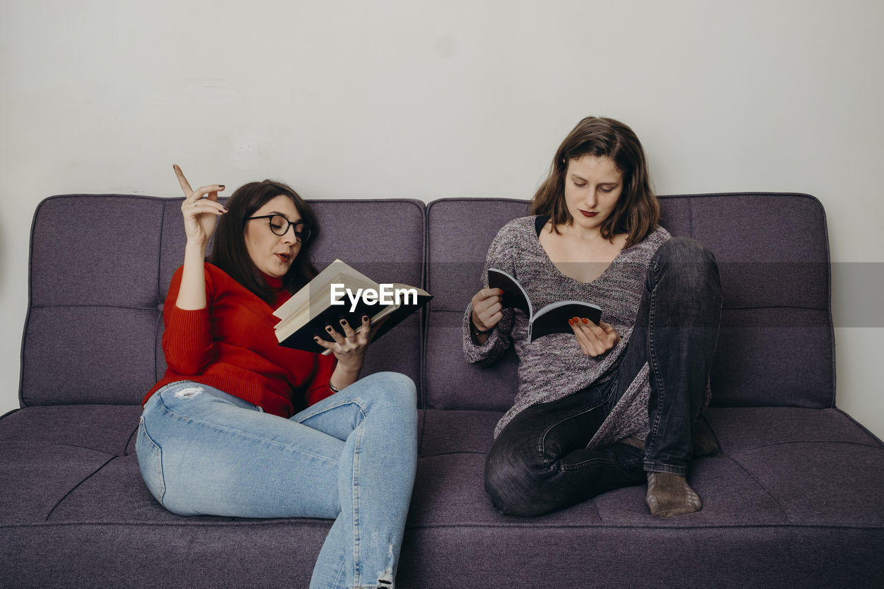 Young females holding book sitting on sofa at home