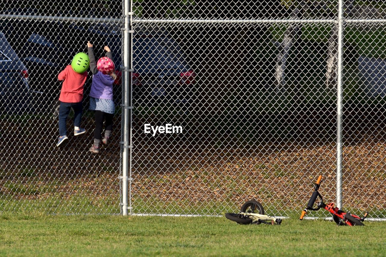 Rear view of siblings climbing on chainlink fence