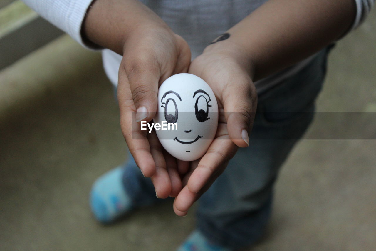 Low section of boy holding anthropomorphic face on egg