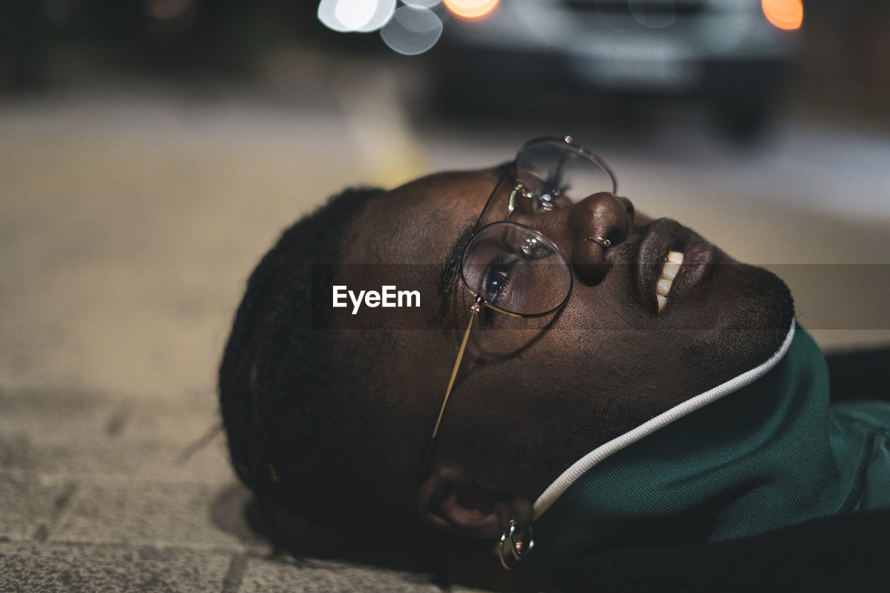 Close-up of thoughtful young man lying down on sidewalk at night