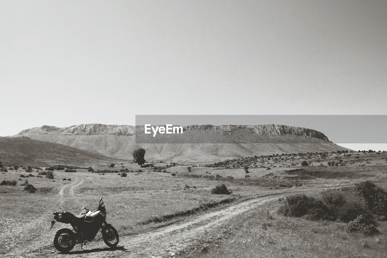 Motorcycle parked on landscape at desert against clear sky