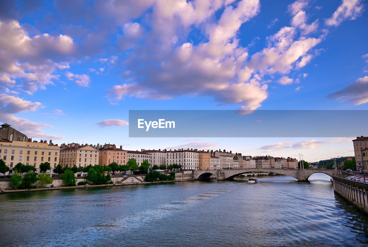 BRIDGE OVER RIVER BY BUILDINGS AGAINST SKY