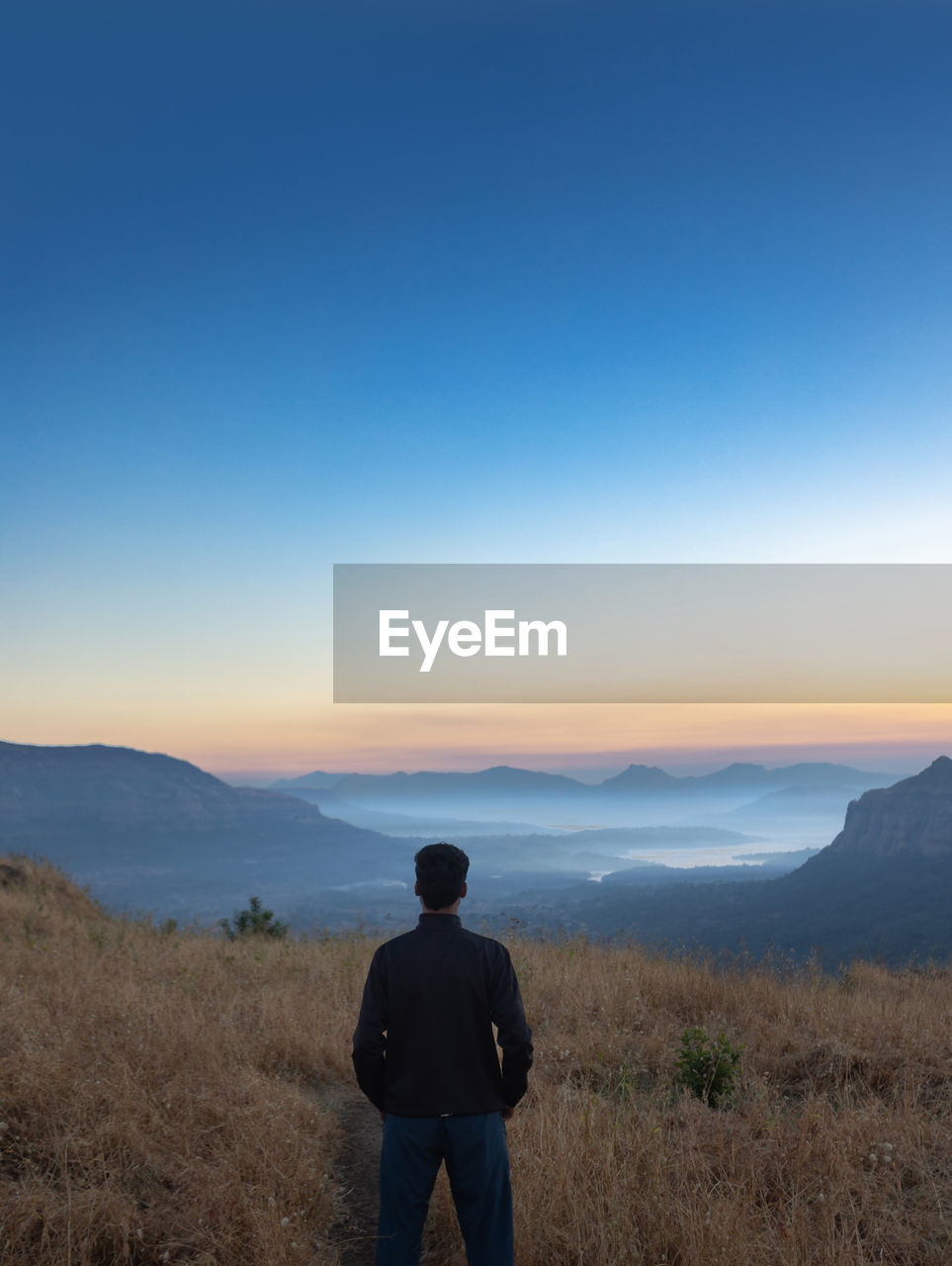 sky, horizon, one person, scenics - nature, landscape, beauty in nature, mountain, nature, rear view, environment, men, wilderness, adult, land, standing, tranquility, blue, leisure activity, tranquil scene, copy space, non-urban scene, mountain range, remote, clear sky, looking at view, travel, outdoors, morning, solitude, three quarter length, ridge, idyllic, vacation, hiking, lifestyles, trip, natural environment, dawn, adventure, cloud, contemplation, holiday, travel destinations, full length, person, silhouette, plant