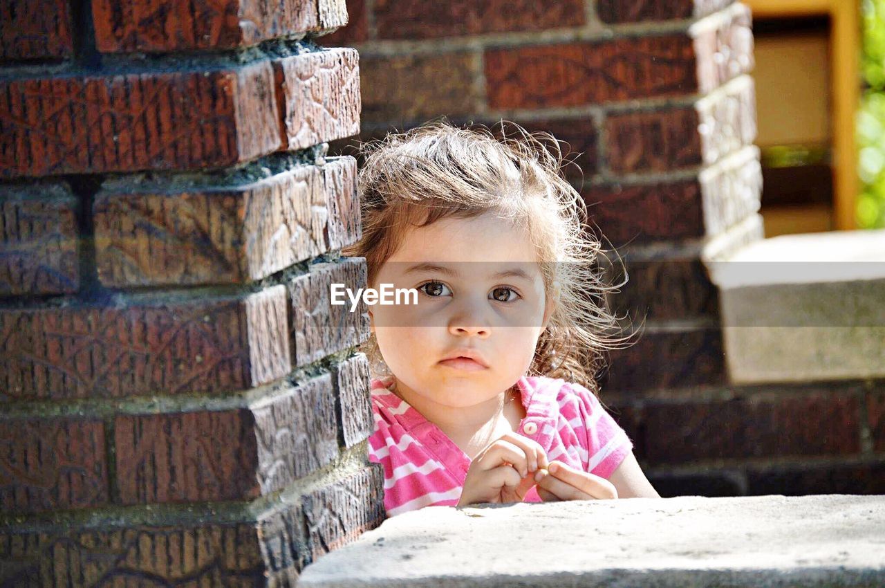 Portrait of cute girl standing by brick wall