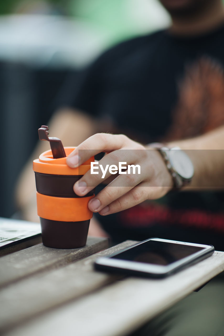 Close-up picture of guy drinking coffee to go on wooden table