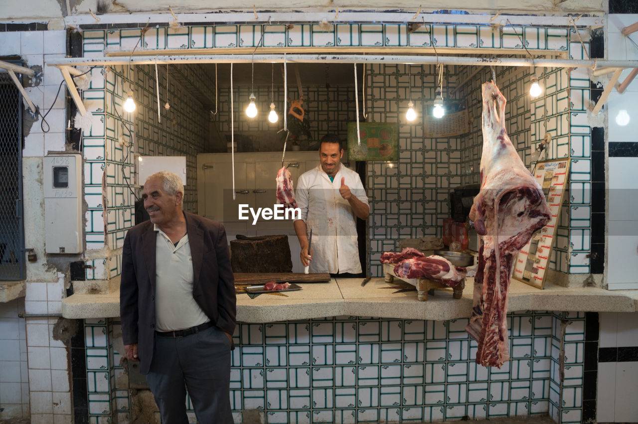 Smiling customer standing by butcher showing thumbs up at shop