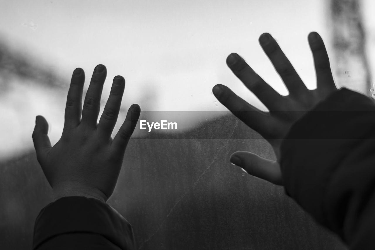 Cropped hands of children touching window