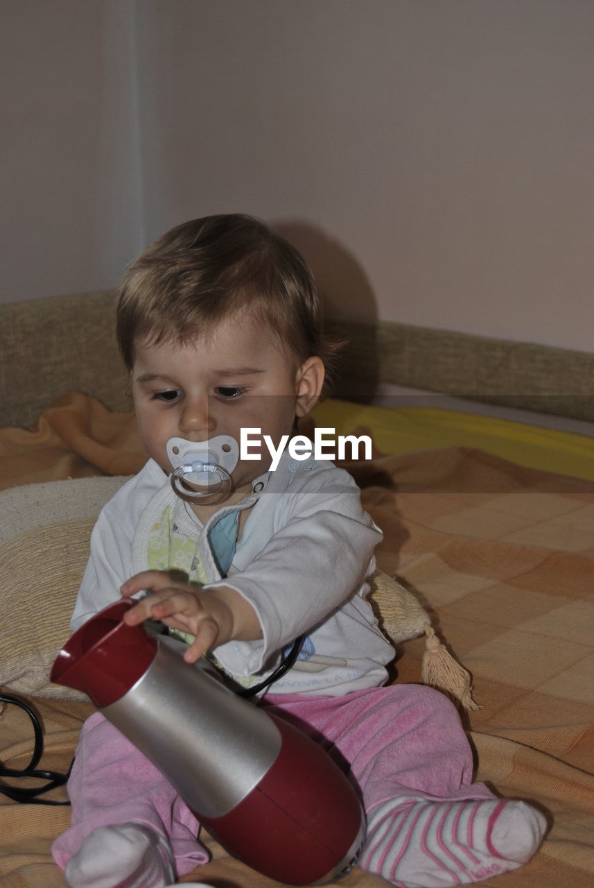 Cute boy holding hair dryer on bed at home