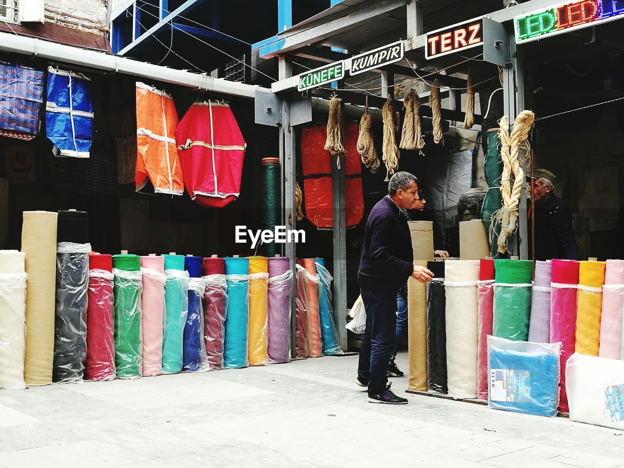 FULL LENGTH OF MAN STANDING ON MULTI COLORED UMBRELLAS IN STREET