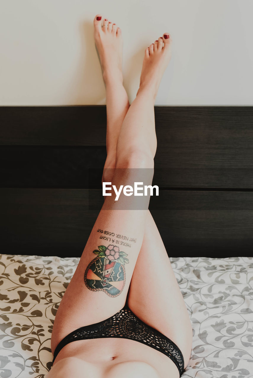 Low section of woman with tattoo on thigh resting at home