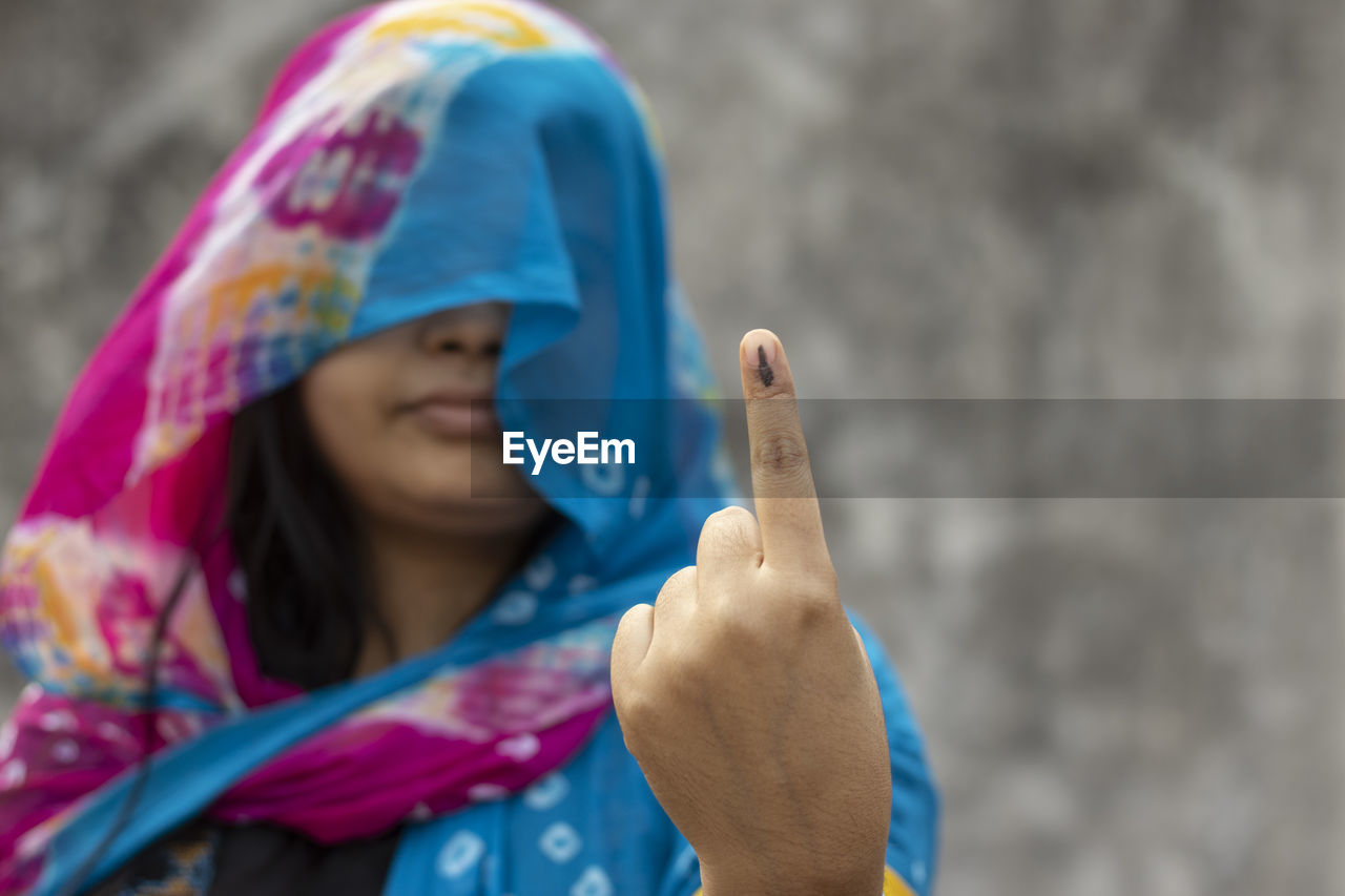 Selective focus on ink-marked finger of an indian village woman behind veil with smiling face