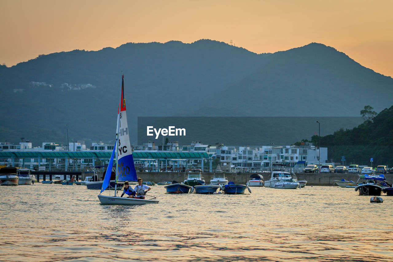 BOATS MOORED ON SEA AGAINST MOUNTAIN RANGE