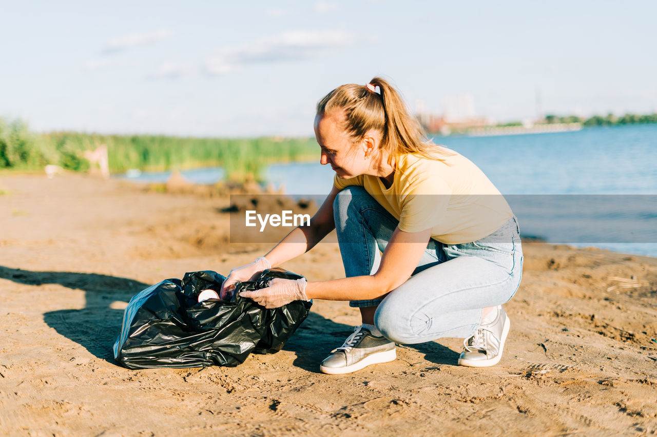 Volunteer satisfied trash, a plastic bottles and coffee cups, clean beach. woman collecting garbage