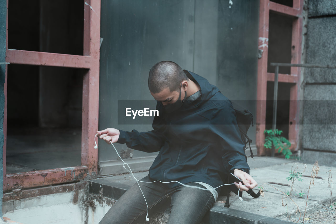 Man holding earphones while sitting against building