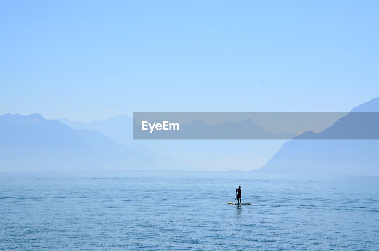 Silhouette person paddleboarding in sea against clear sky