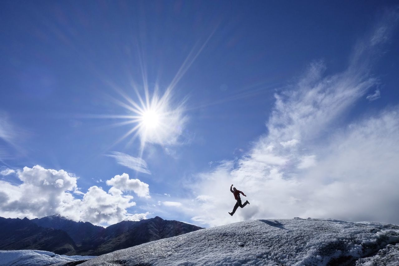 Silhouette man jumping on snow against bright blue sky