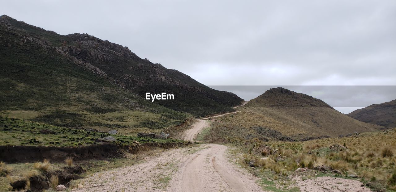 Dirt road leading towards mountains against sky