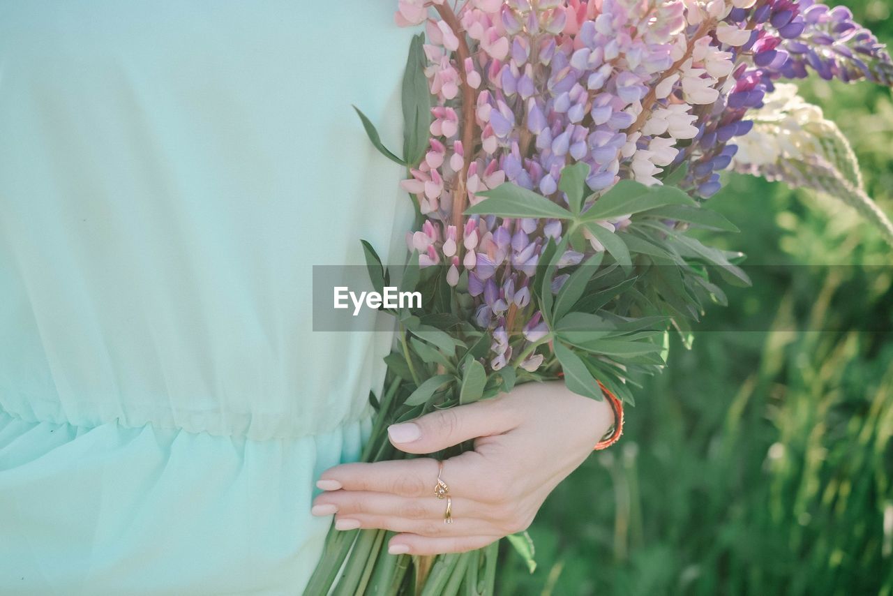 Midsection of woman with purple flowers on field