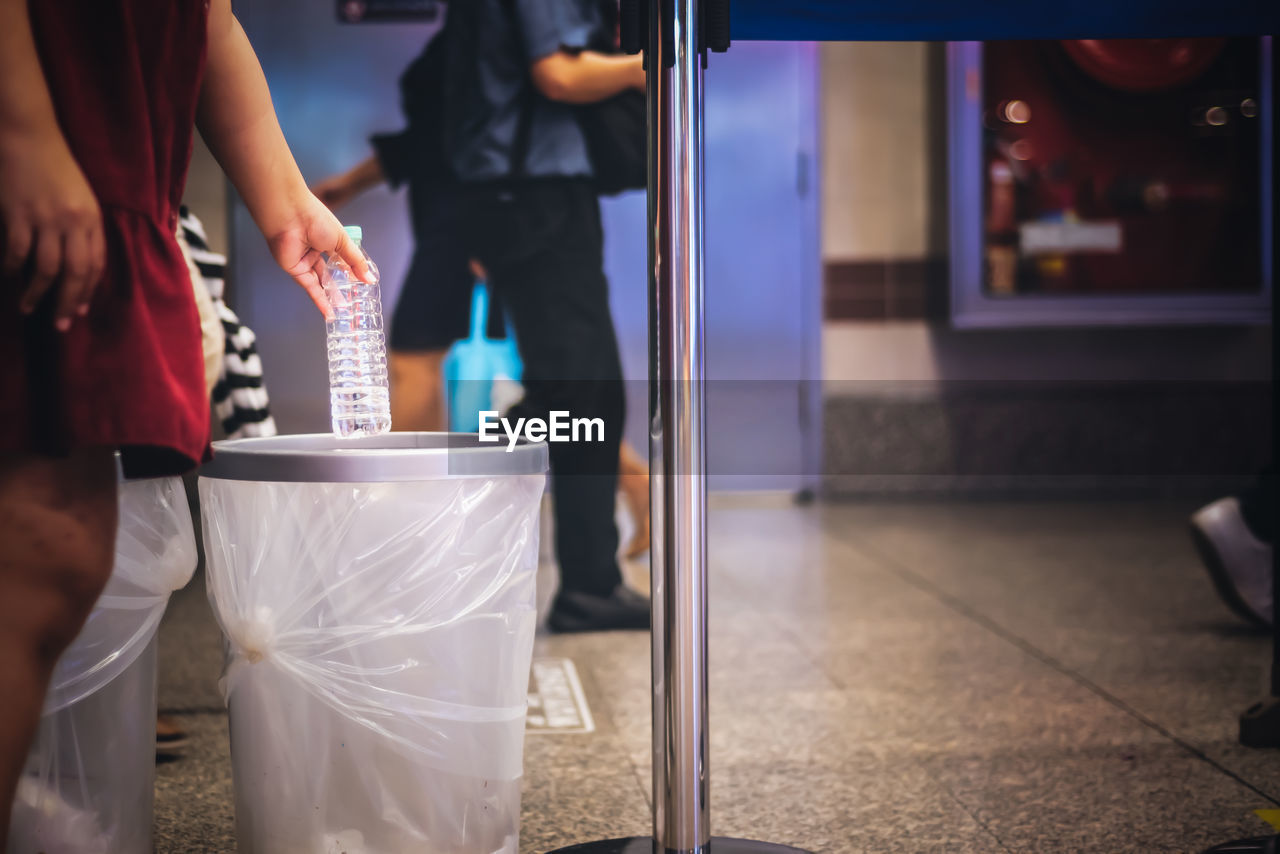 Midsection of woman holding bottle over dustbin on floor