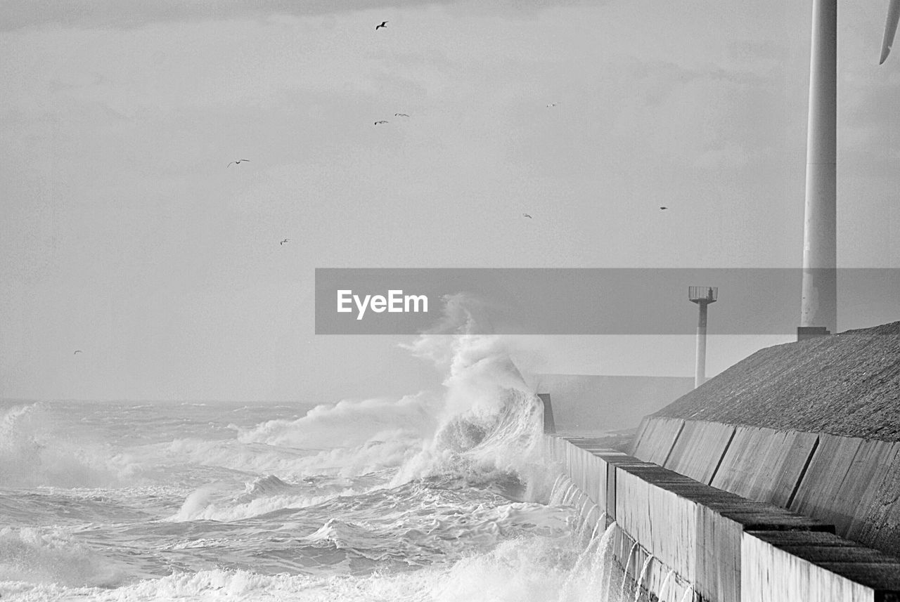 Sea waves splashing on shore against sky