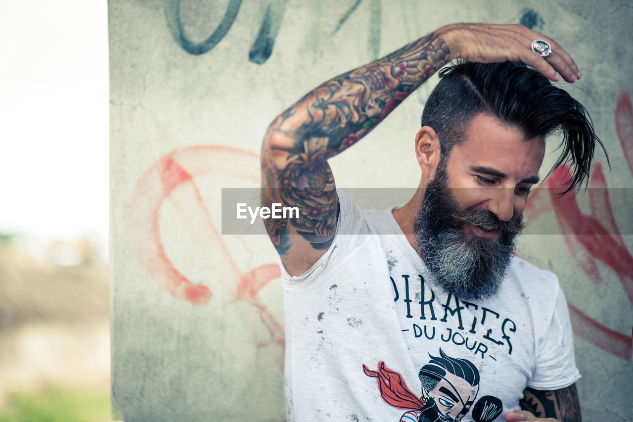 Happy man with tattoo on hands standing against wall