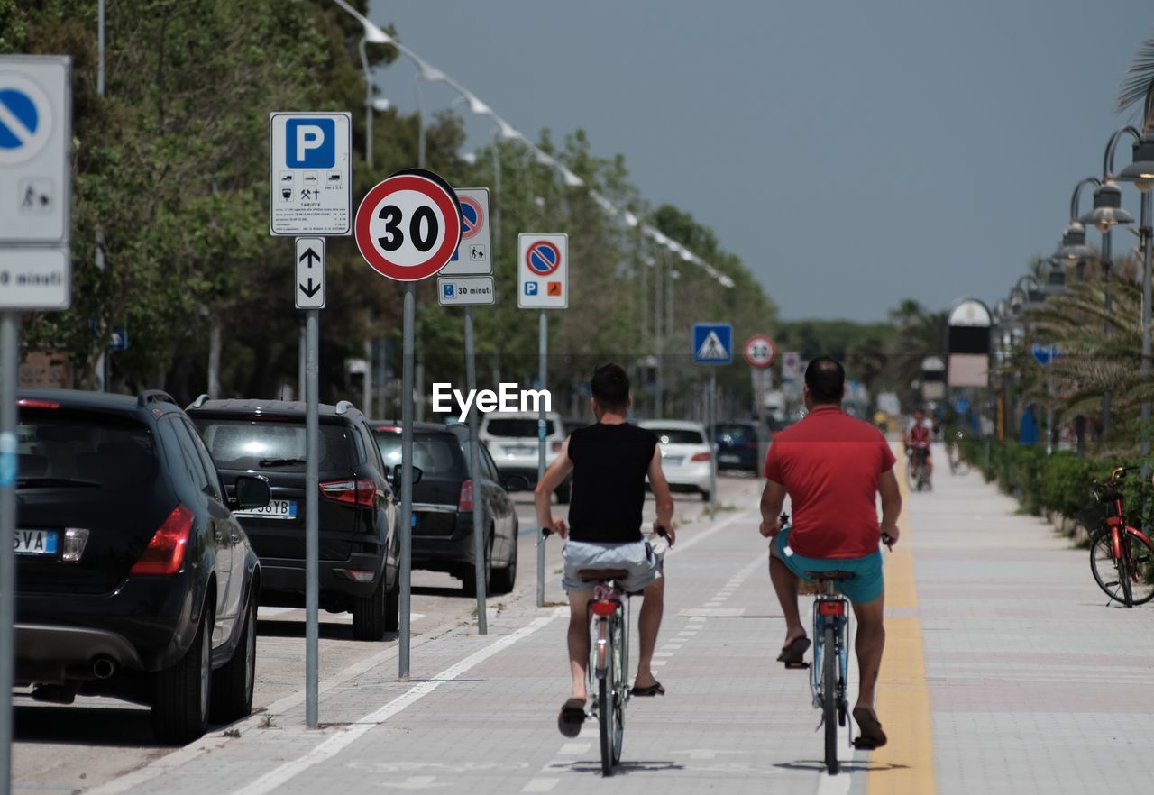 REAR VIEW OF PEOPLE RIDING BICYCLE ON ROAD