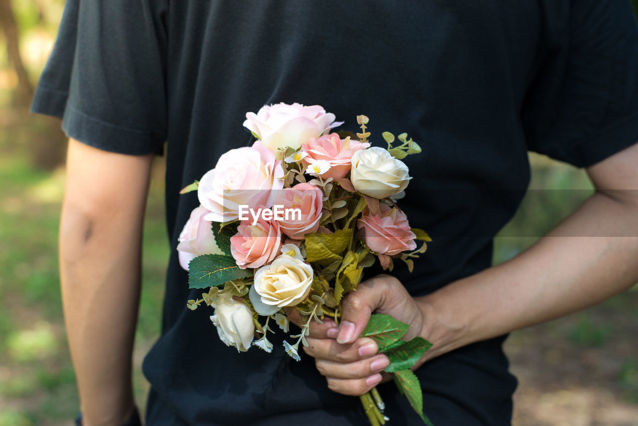 Midsection of man holding rose bouquet behind his back outdoors