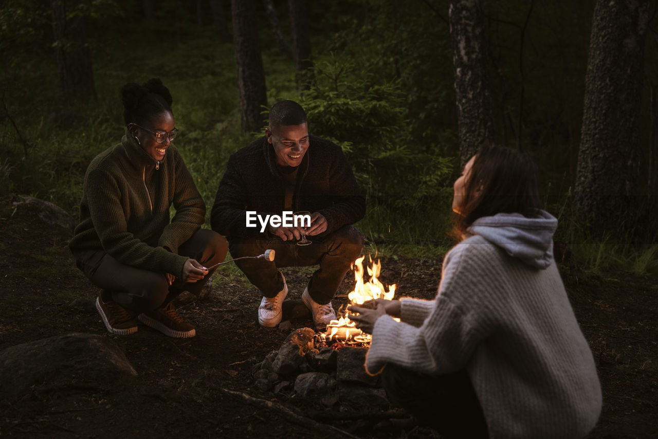 Friends sitting by campfire in forest