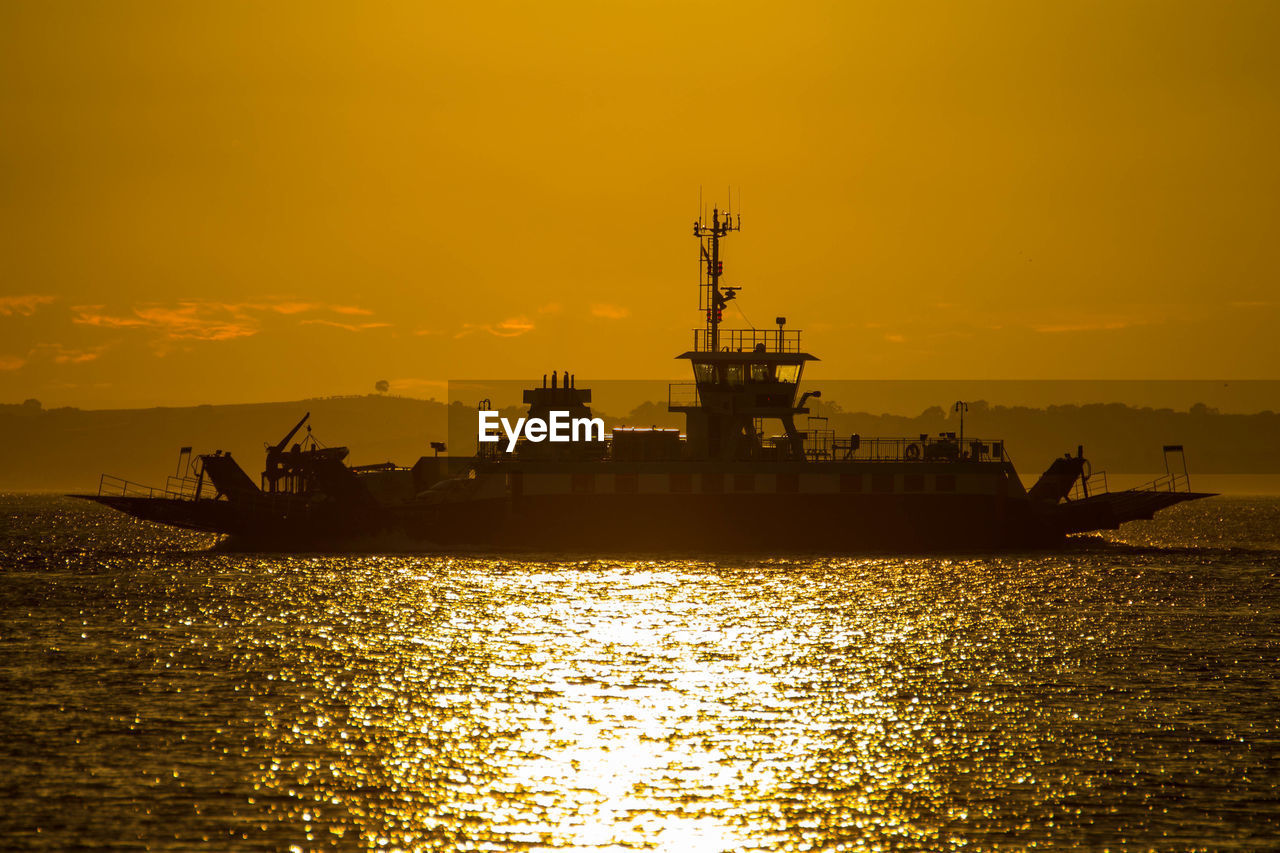 Silhouette cranes by sea against sky during sunset