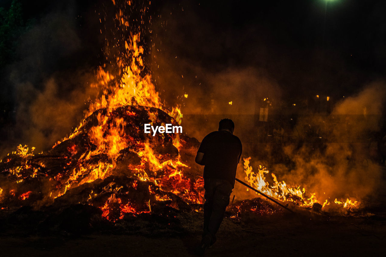 Rear view of man standing by fire at night