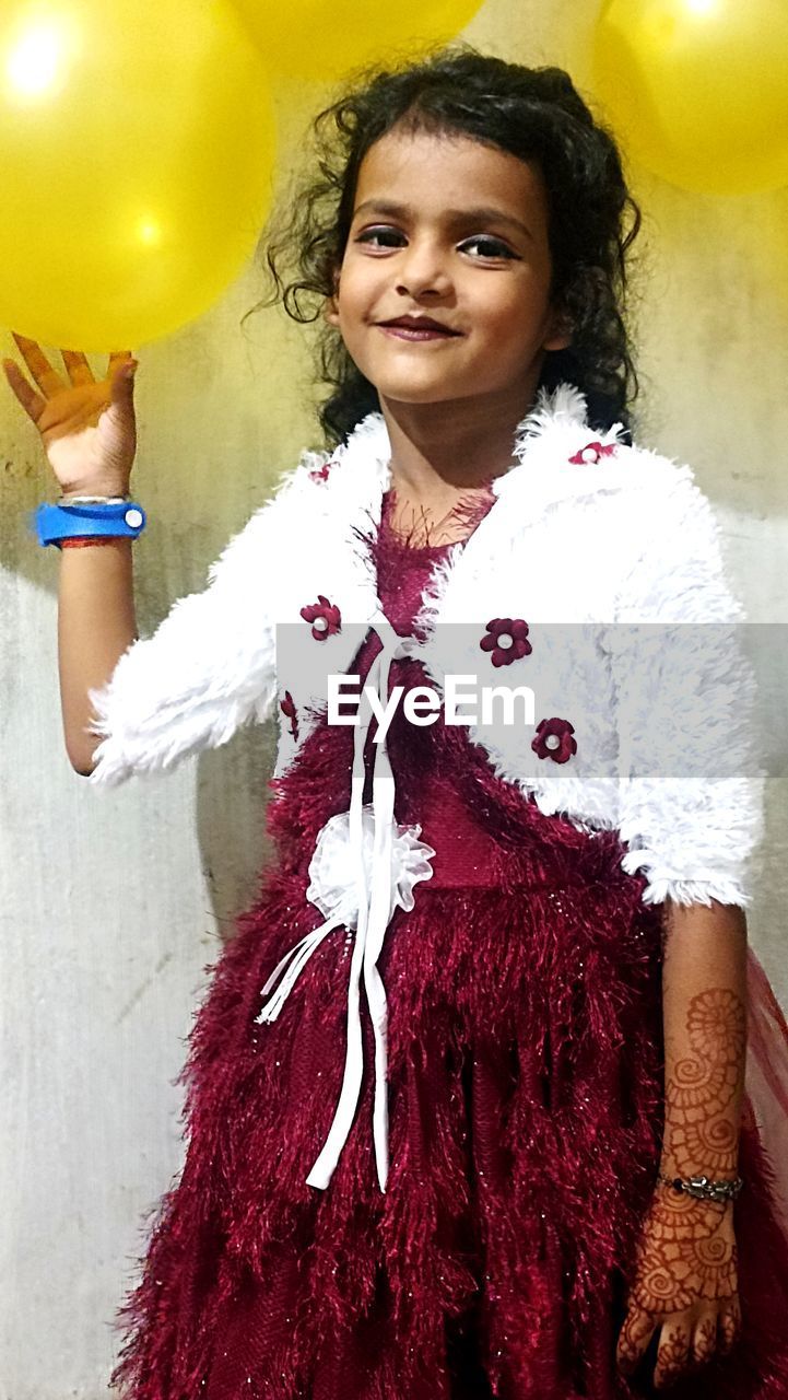 one person, portrait, women, looking at camera, celebration, smiling, female, clothing, balloon, happiness, adult, event, child, emotion, indoors, person, childhood, hairstyle, toy, costume, waist up, standing, fashion, dress, arts culture and entertainment, front view, cheerful, cute, fun, holding, young adult, human face