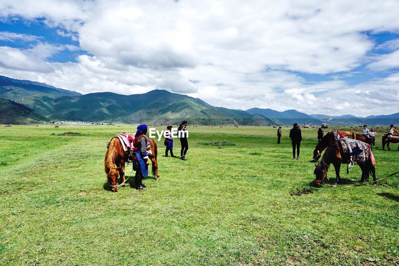 TOURISTS ON FIELD AGAINST MOUNTAINS