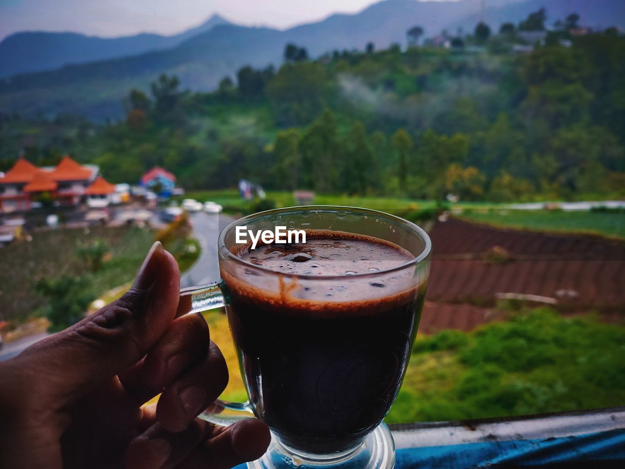 Midsection of person holding drink against mountains