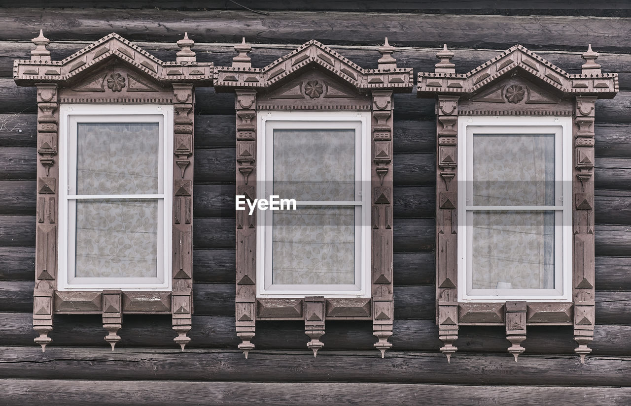 Wndows with carved wooden architraves. log facade of typical rural russian house.