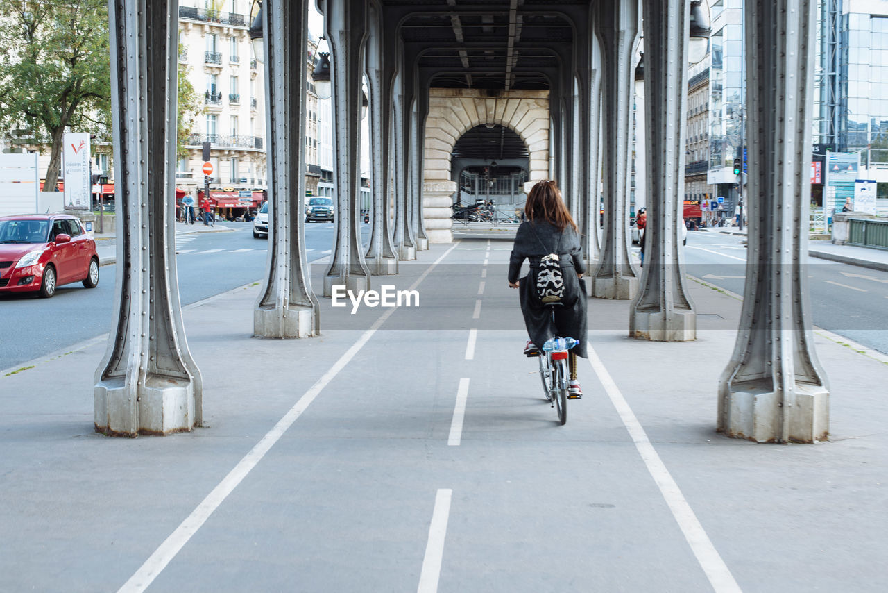 Rear view of woman riding bicycle under bridge