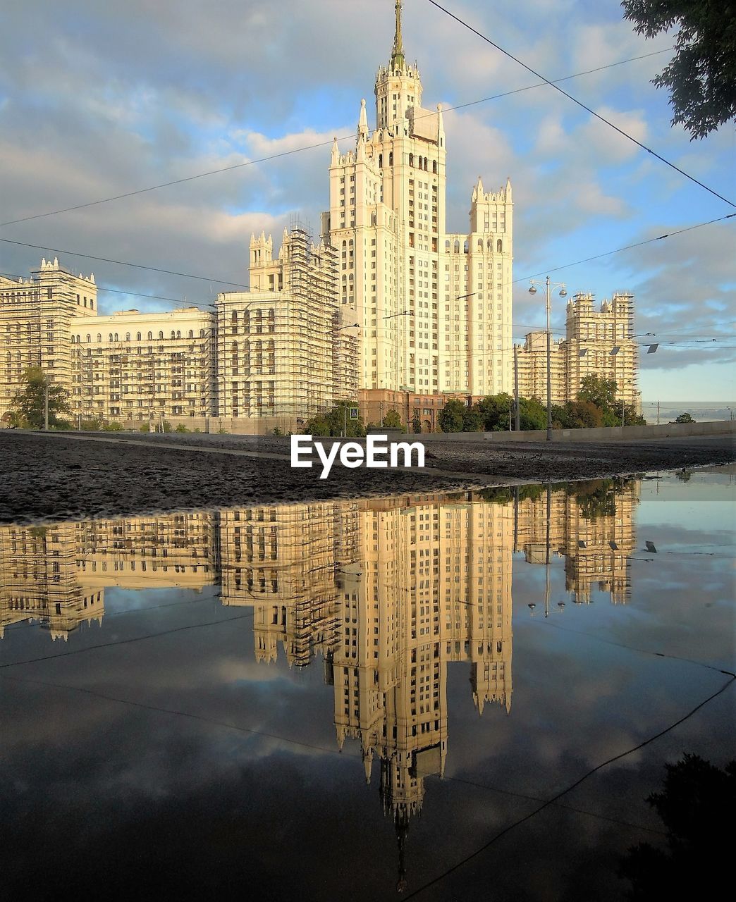 Modern buildings with reflection on puddle against cloudy sky