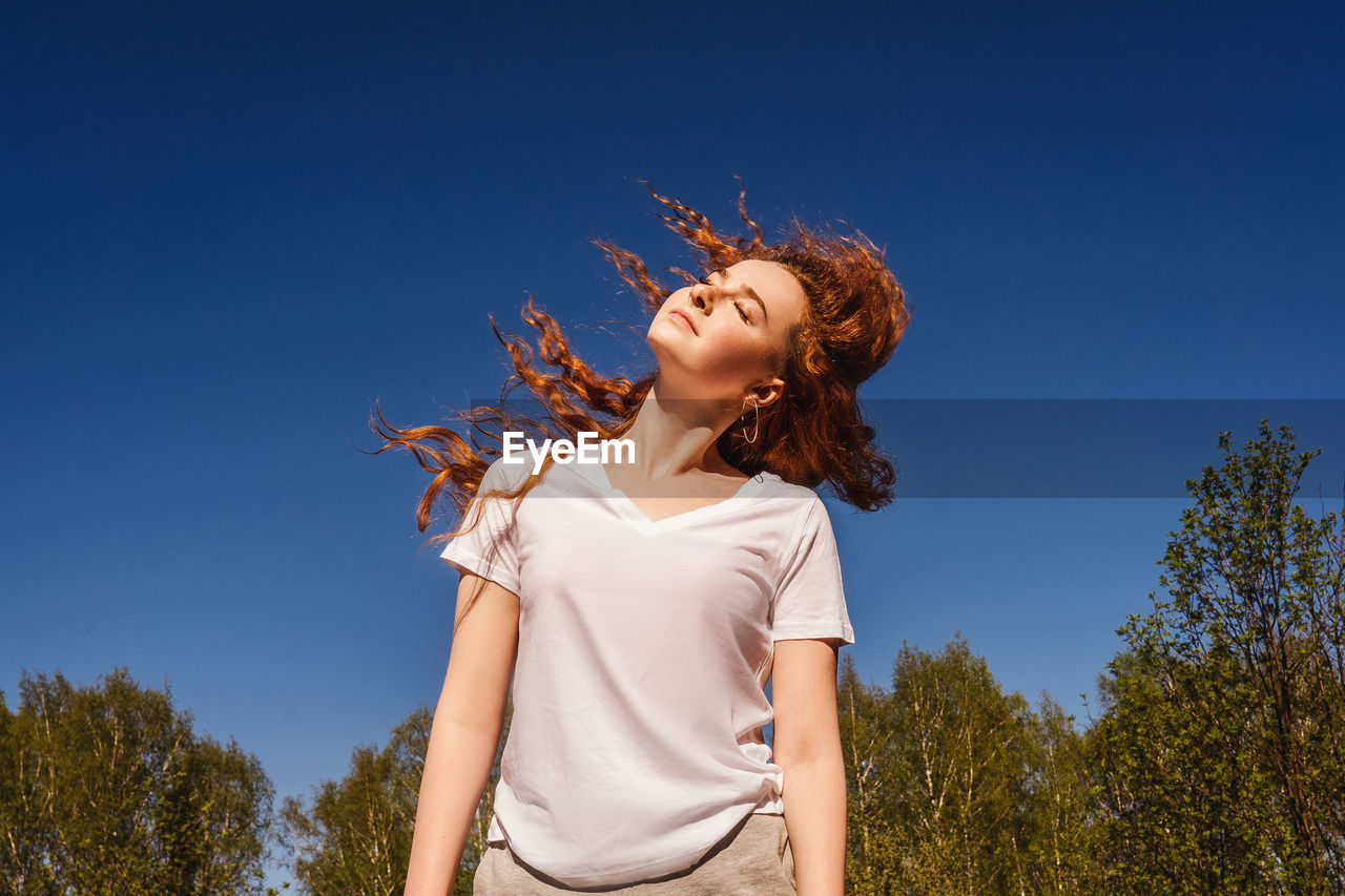 Low angle view of girl tossing hair against sky