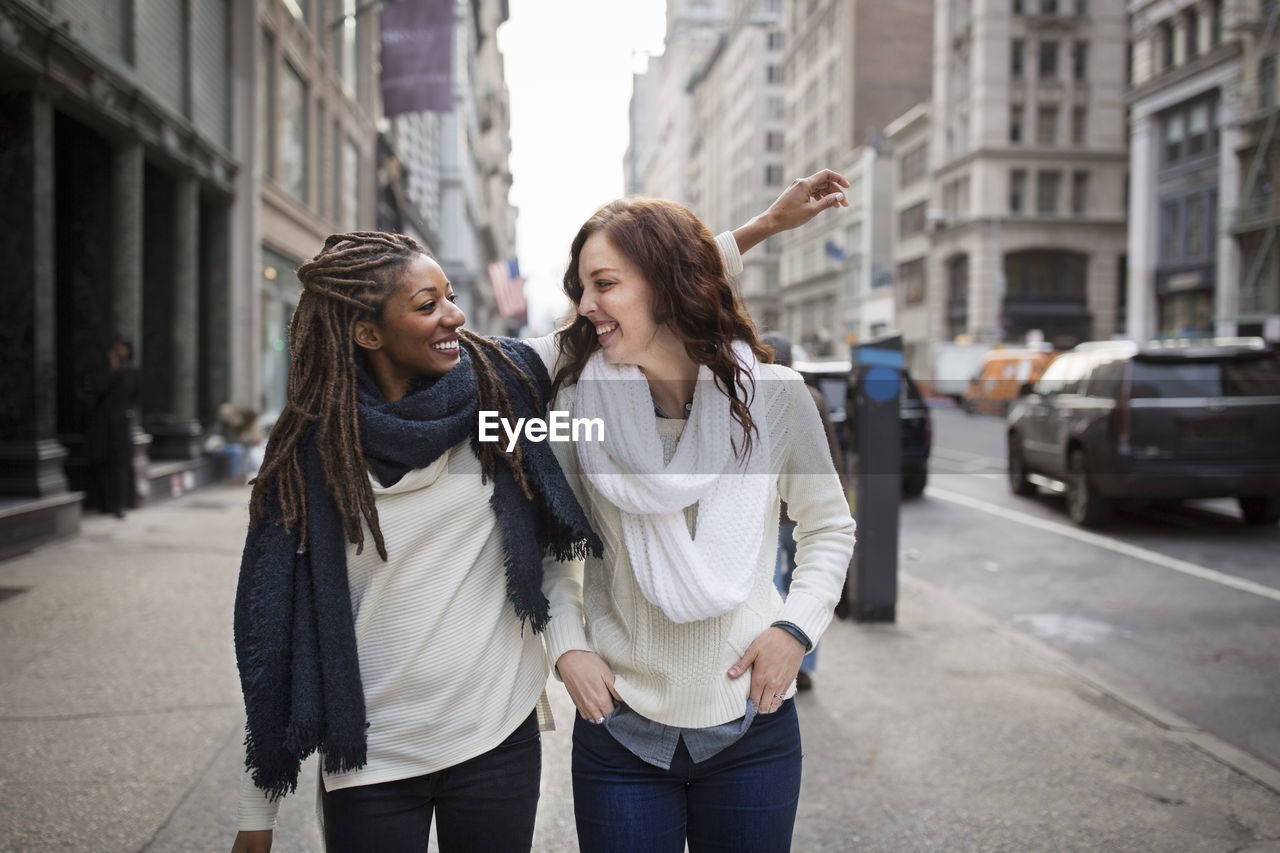 Female friends smiling and enjoying while standing on footpath