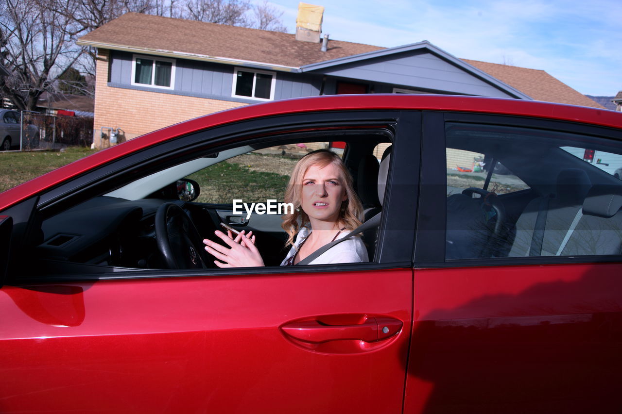 Woman sitting in red car during sunny day