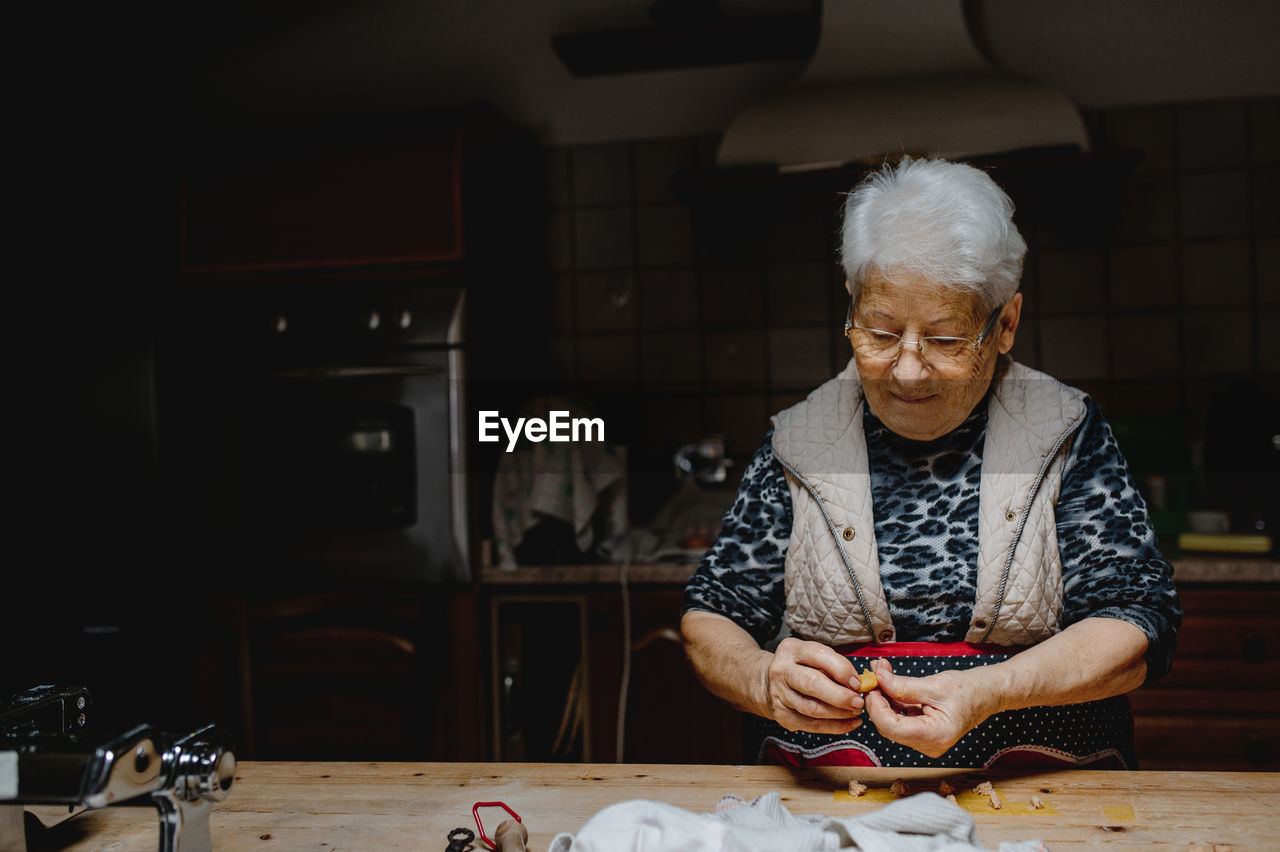 Aged housewife preparing delicious homemade tortellini while standing at table in kitchen at home