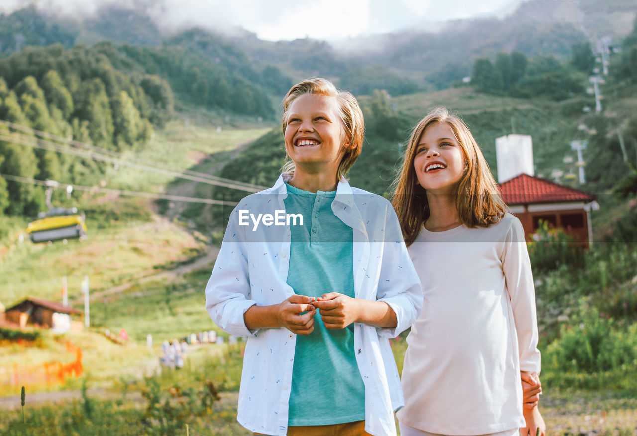 Portrait of smiling sibling standing against mountain