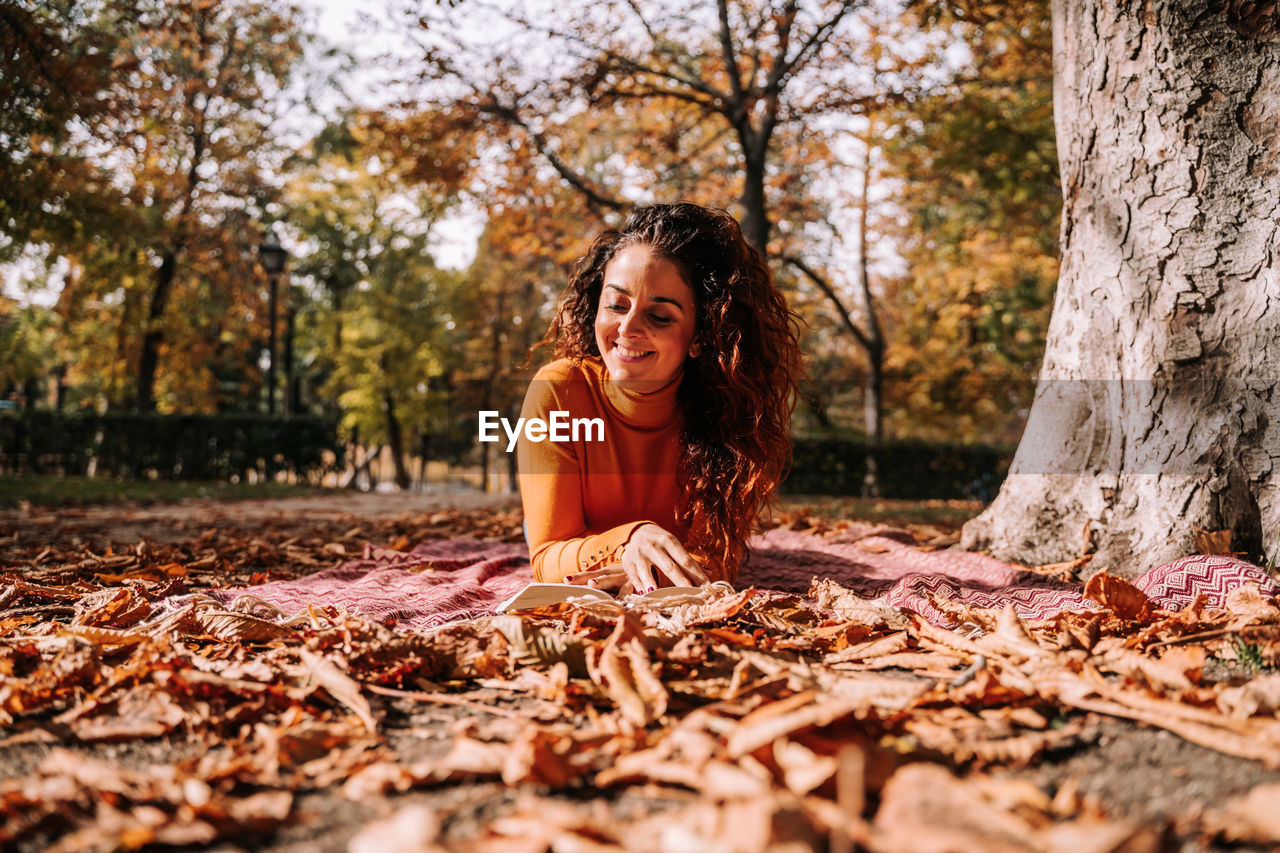 Smiling woman reading book while lying down at park