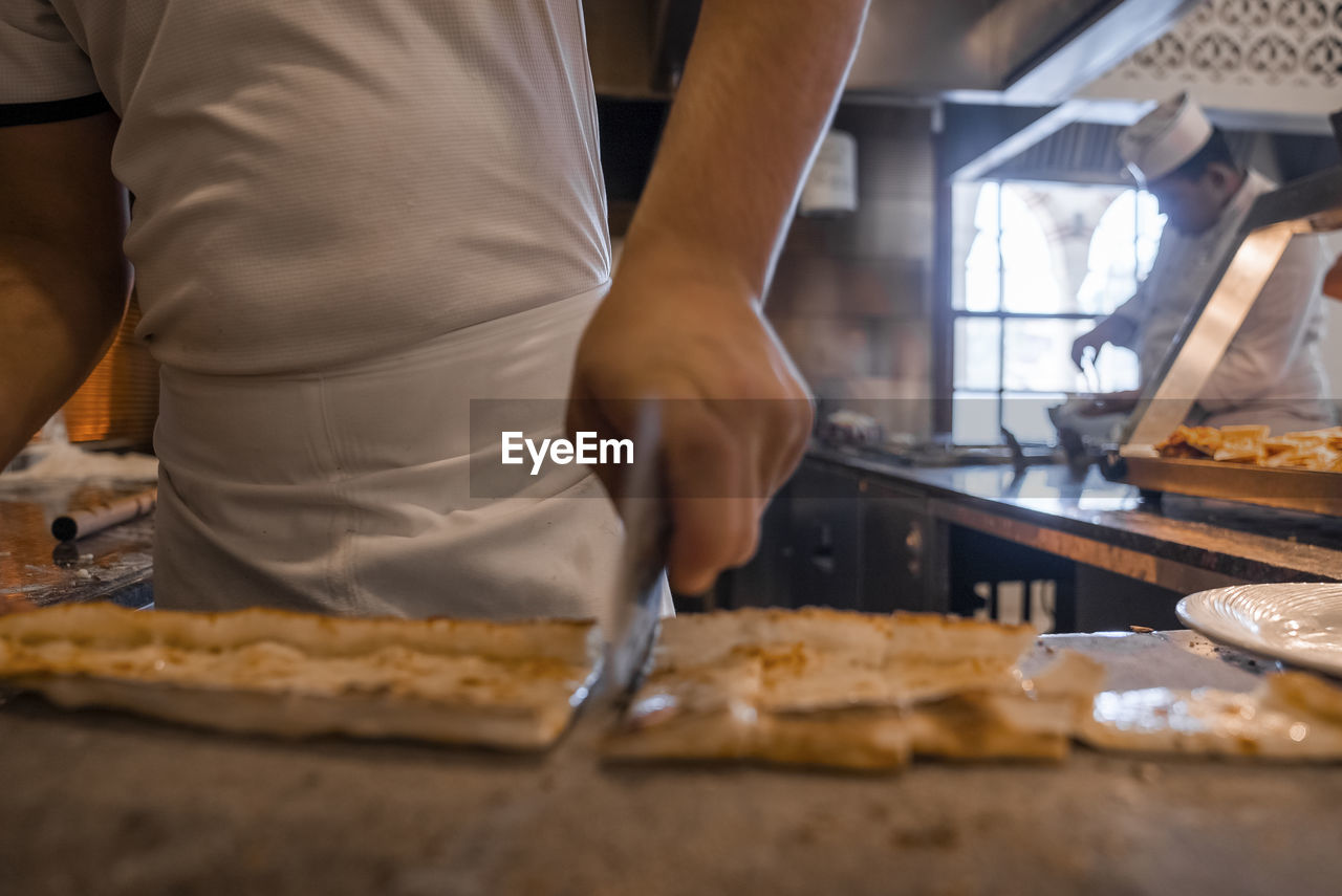 Chef cutting turkish pide into slices on table at restaurant